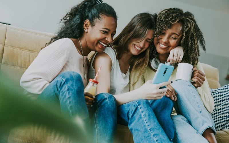 a group of women sitting on a couch looking at a cell phone